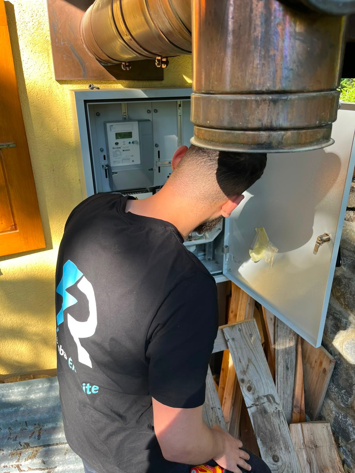 Électricien Renobat en t-shirt floqué, intervention sur un coffret de comptage électrique en Valais.